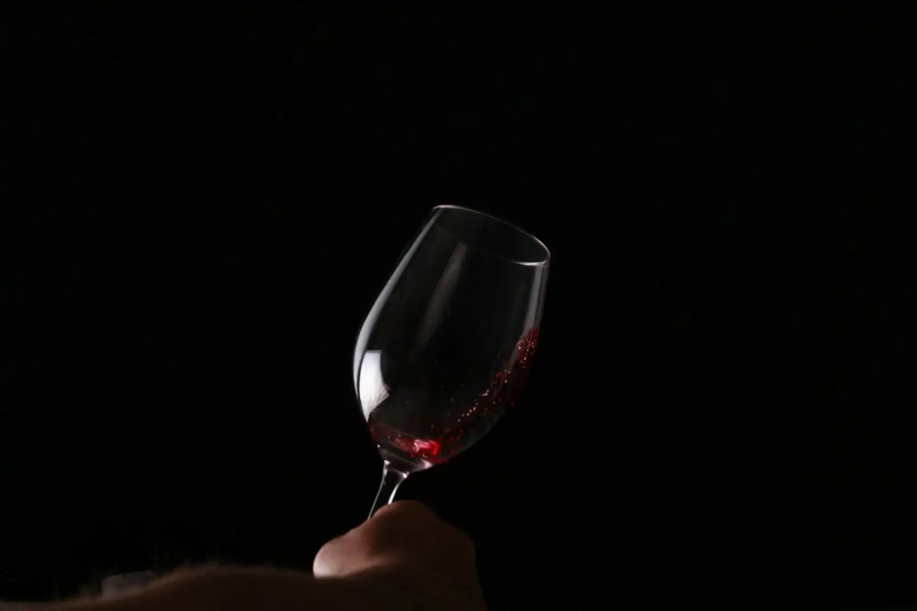 A hand raising a glass of red wine in the dark